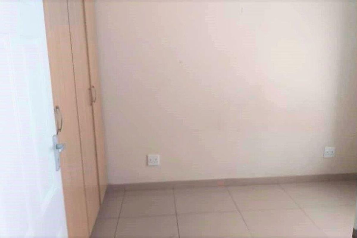 A simple, empty bedroom featuring light-colored floor tiles and built-in wooden cupboards.
