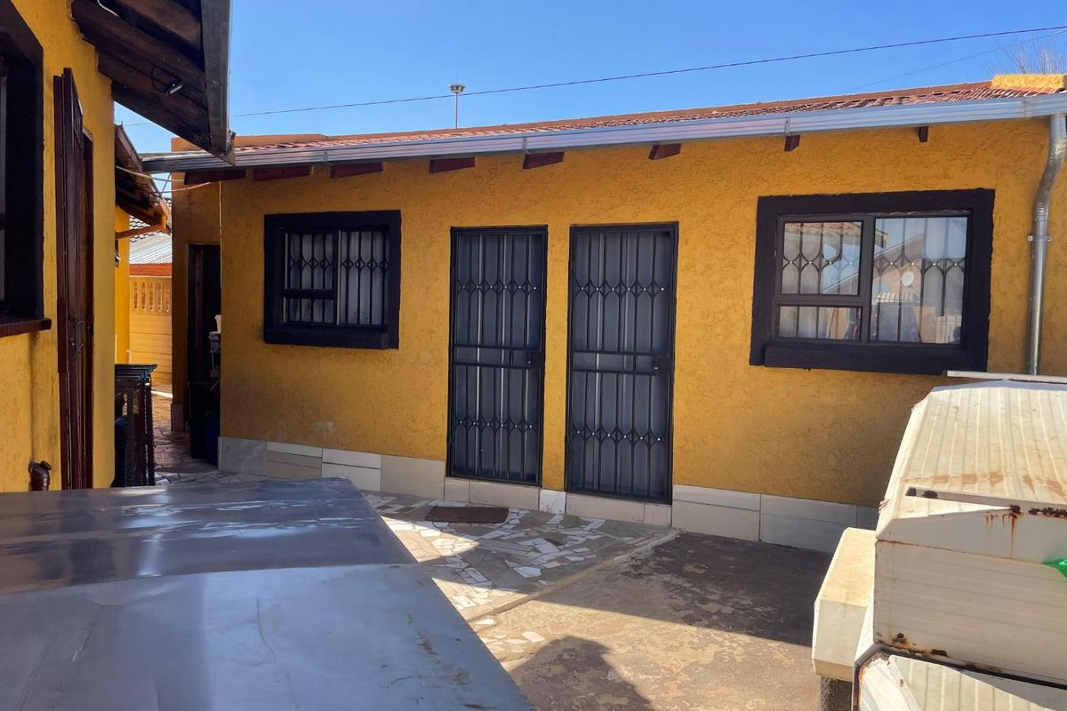 Rear exterior view of the property featuring a paved patio area, security gates, and exposed roof rafters.