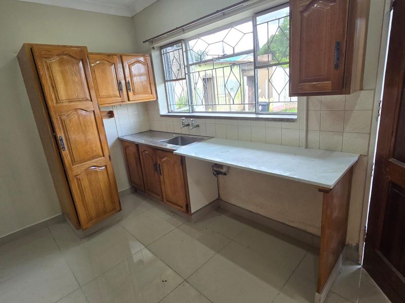 A dated kitchen featuring wooden cabinetry, a stainless steel sink, and tiled flooring, offering a functional layout ready for modernization.