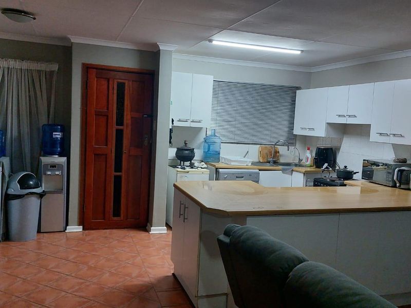 Open plan kitchen area featuring white cabinetry, laminate countertops, tiled flooring, and direct access to an adjacent room via a timber door.