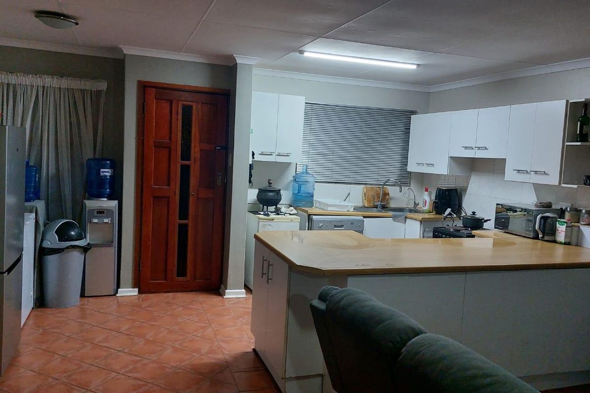 Open plan kitchen area featuring white cabinetry, laminate countertops, tiled flooring, and direct access to an adjacent room via a timber door.