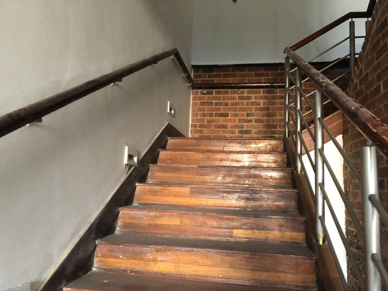 A staircase featuring wooden treads, exposed brick accents, and stainless steel handrails, providing access between levels in this retail property.