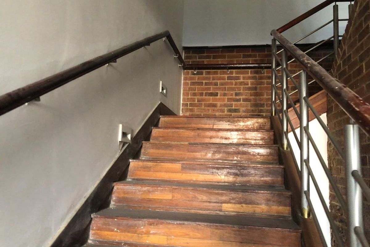 A staircase featuring wooden treads, exposed brick accents, and stainless steel handrails, providing access between levels in this retail property.