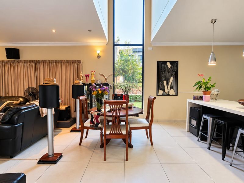 Spacious open-plan living and dining area featuring tiled floors, a breakfast bar with pendant lighting, and a large full-height window providing natural light.