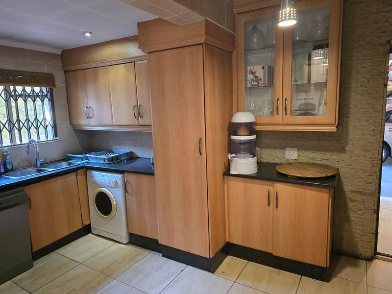 A functional kitchen featuring wood-finish cabinetry, granite countertops, tiled flooring, and integrated laundry appliances with ample storage space.