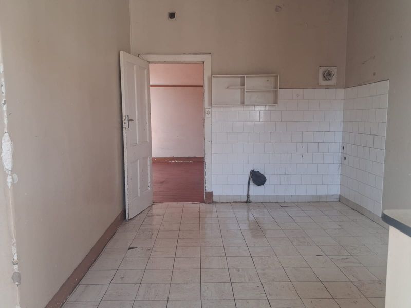 An empty, dated kitchen area featuring tiled flooring, a tiled splashback, and wall-mounted shelving, requiring significant renovation and cosmetic updates.