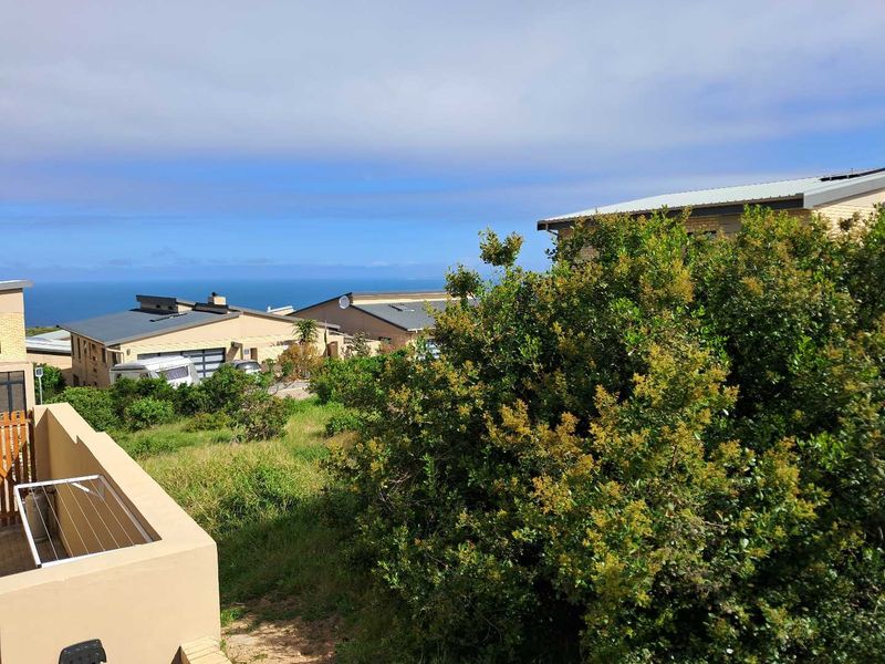 An elevated view overlooking a residential neighborhood with a distant coastal horizon and natural vegetation.