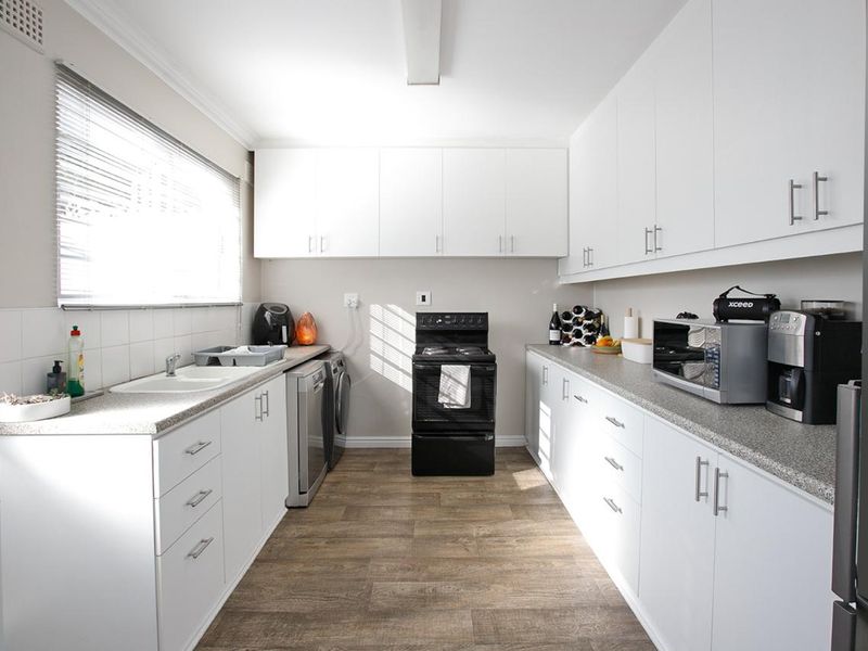 A functional galley-style kitchen featuring white cabinetry, laminate countertops, a freestanding stove, and wood-look laminate flooring.
