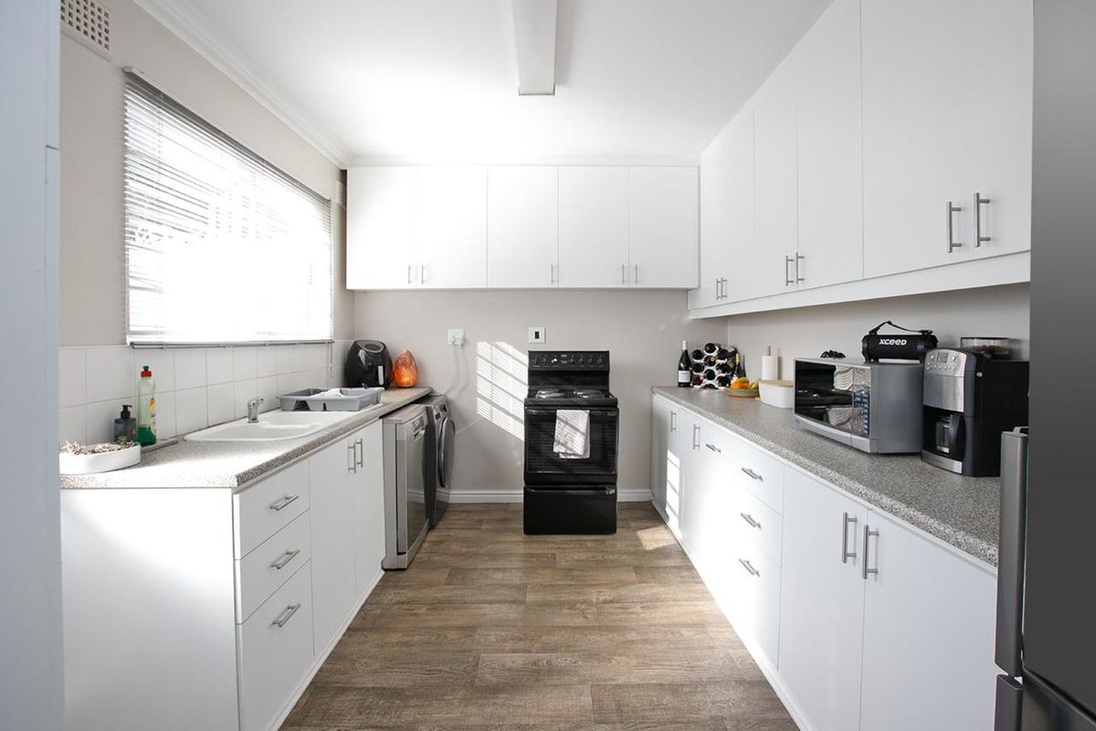 A functional galley-style kitchen featuring white cabinetry, laminate countertops, a freestanding stove, and wood-look laminate flooring.
