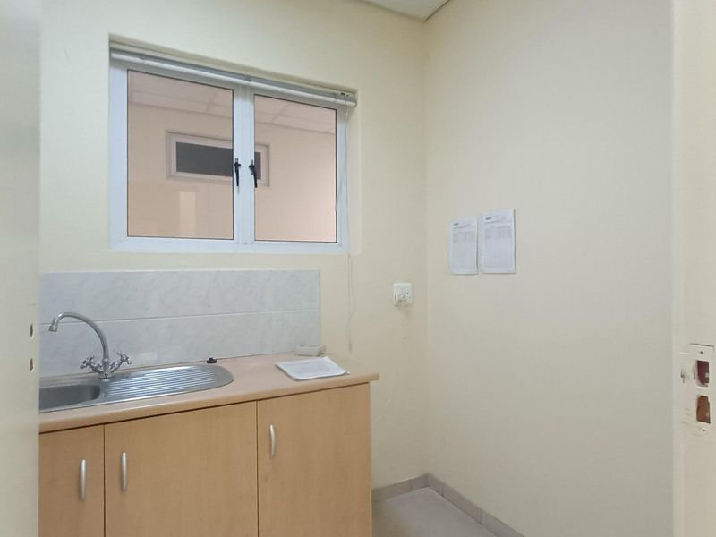 A functional scullery or kitchenette area featuring a stainless steel sink, laminate cabinetry, and tiled splashback.