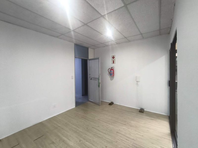 A vacant office space featuring a suspended ceiling, laminate flooring, and integrated safety equipment including a fire extinguisher and intercom system.