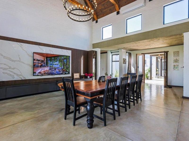 Spacious open-plan living and dining area featuring high vaulted timber ceilings, polished concrete floors, and a sophisticated stone-clad media wall.
