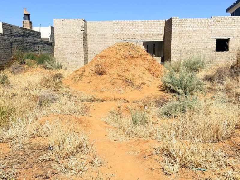 Rear view of a property under construction featuring unrendered masonry walls and an undeveloped garden area with a large soil mound.