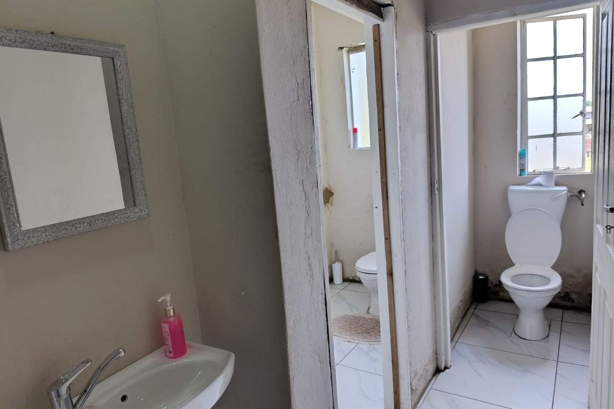 A functional bathroom area featuring a wall-mounted basin and two separate toilet cubicles with tiled flooring and basic sanitary fixtures.