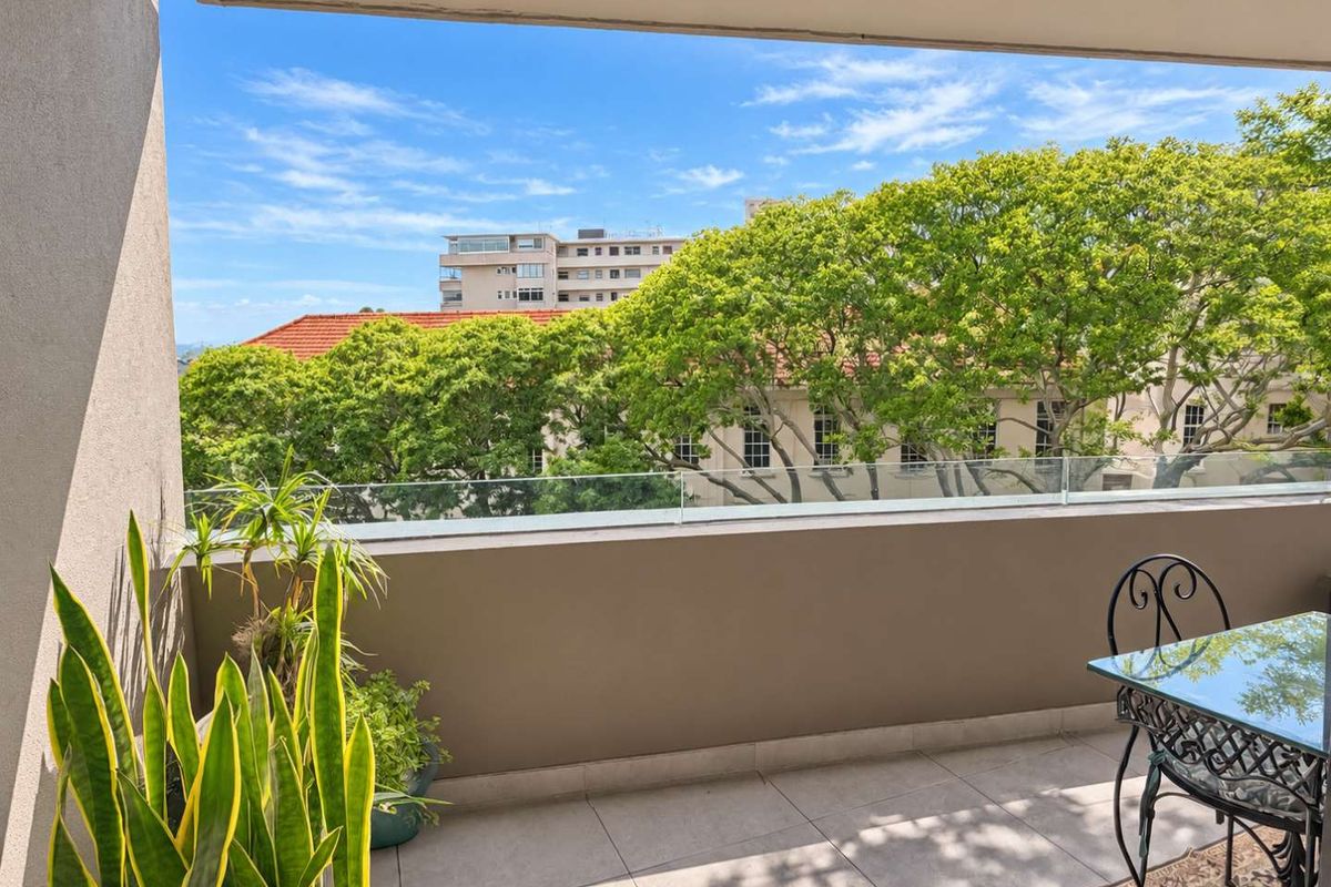 A well-maintained balcony featuring a modern glass balustrade and tiled flooring, offering an open view of the surrounding neighborhood and mature trees.