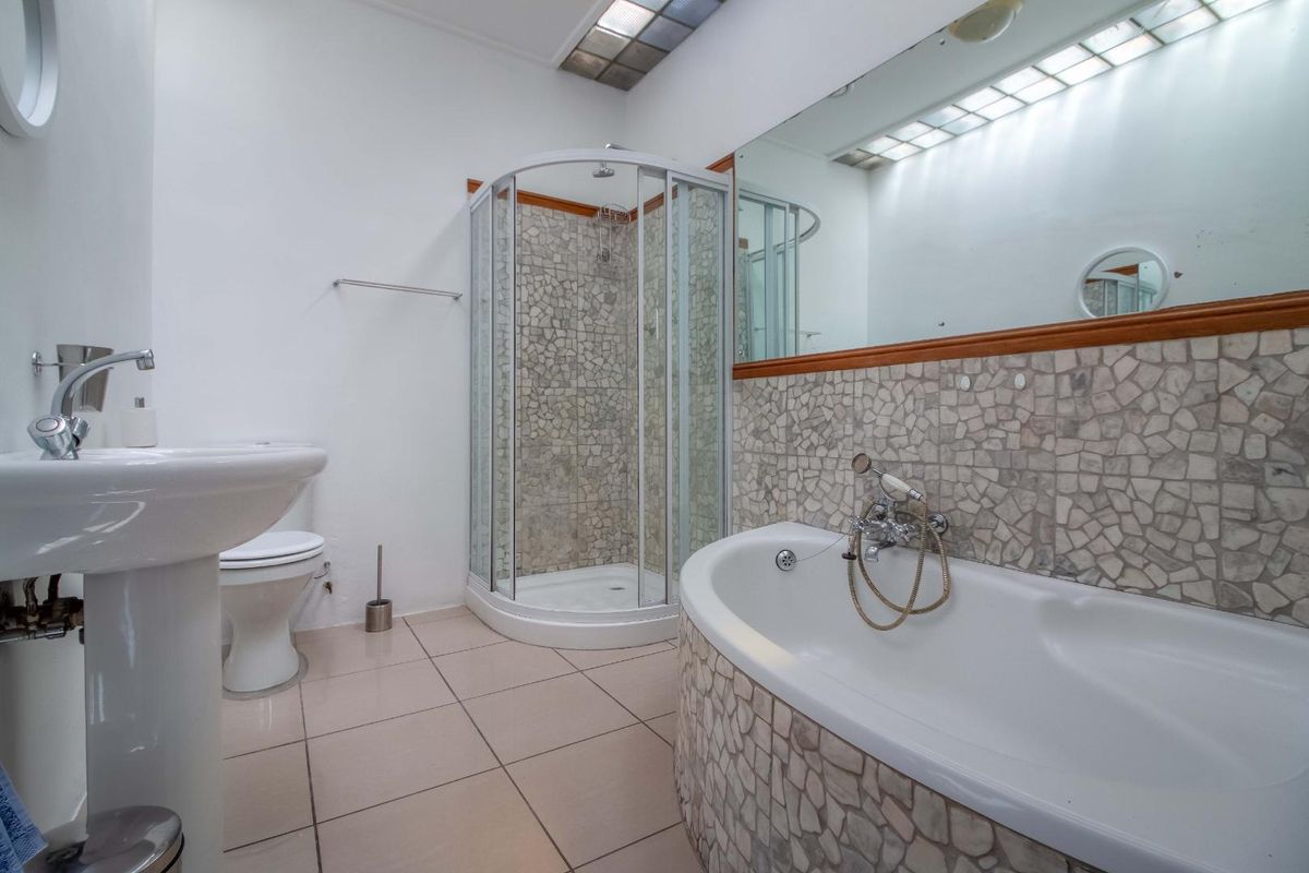 A functional bathroom featuring a corner shower enclosure, a bathtub with mosaic tile surround, a pedestal basin, and a large wall-mounted mirror.