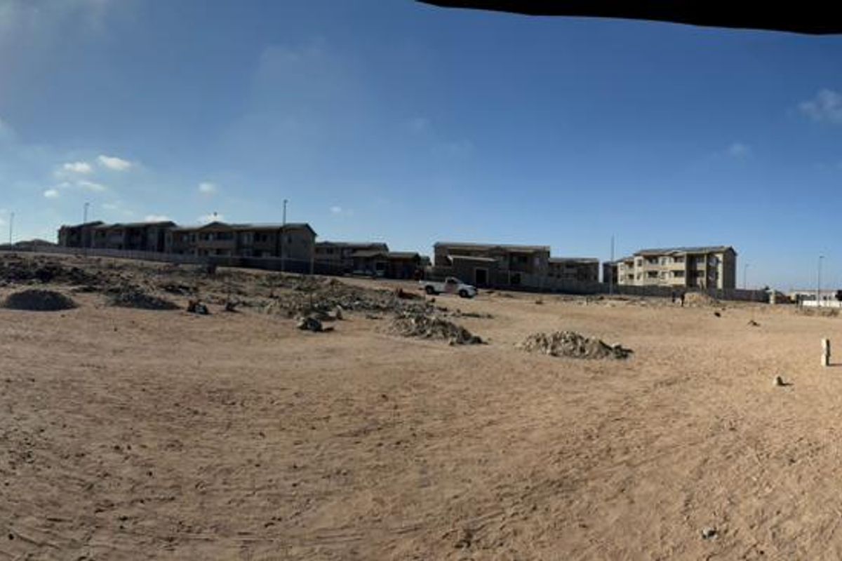 A wide panoramic view of an undeveloped plot of land with surrounding residential buildings in the distance.