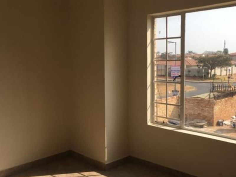 A bright, empty bedroom featuring tiled flooring, neutral walls, and a large window with security bars, offering a clear view of the surrounding neighborhood.