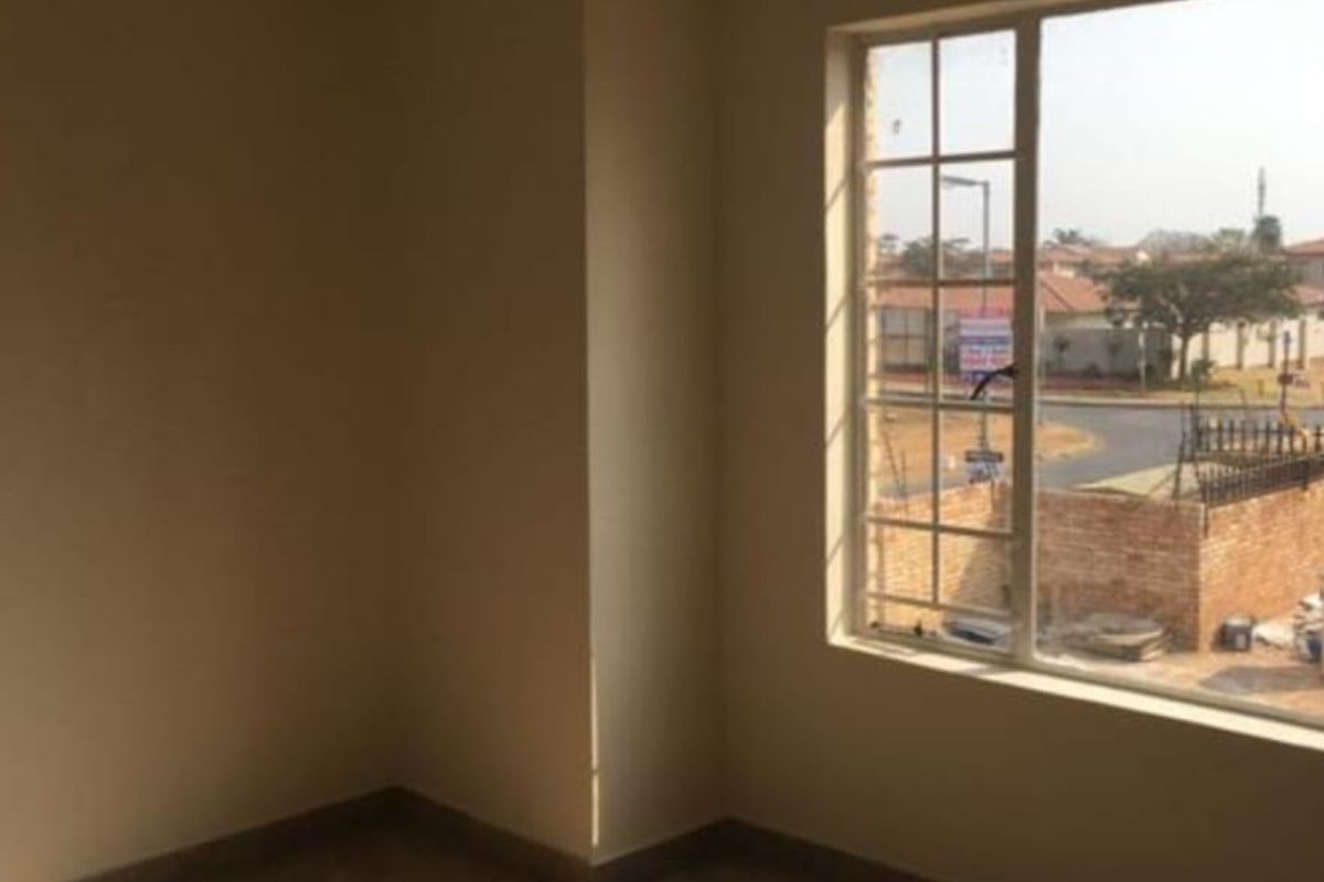 A bright, empty bedroom featuring tiled flooring, neutral walls, and a large window with security bars, offering a clear view of the surrounding neighborhood.