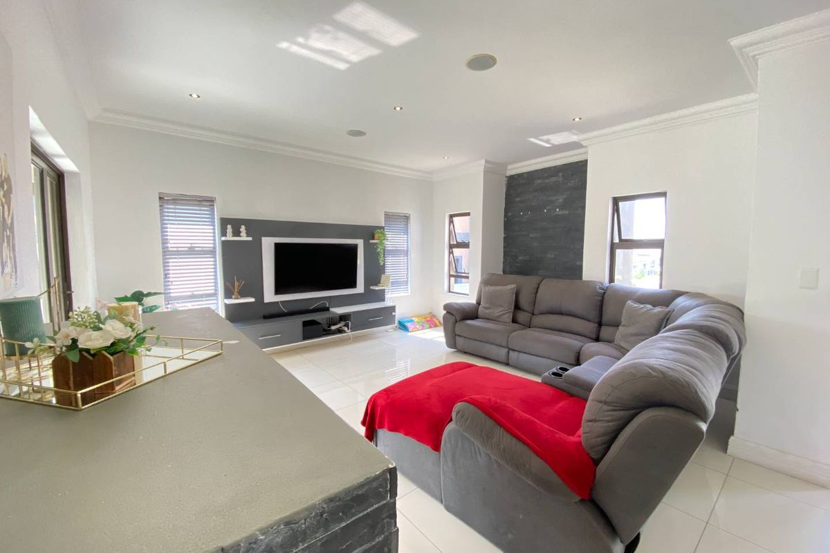 Spacious living room featuring a modern built-in media unit, stone feature wall, tiled flooring, and recessed lighting with ample natural light.