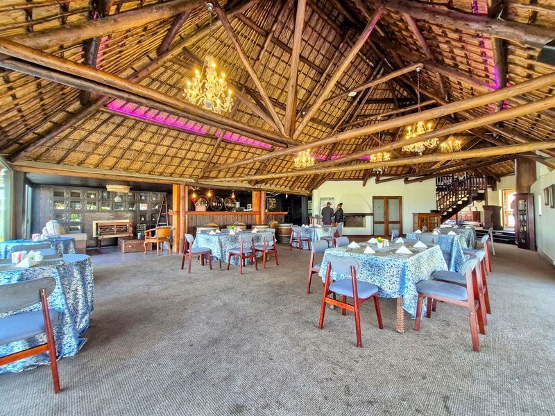 Spacious open-plan entertainment area featuring a high thatched roof with exposed timber trusses, a built-in bar, fireplace, and a staircase.