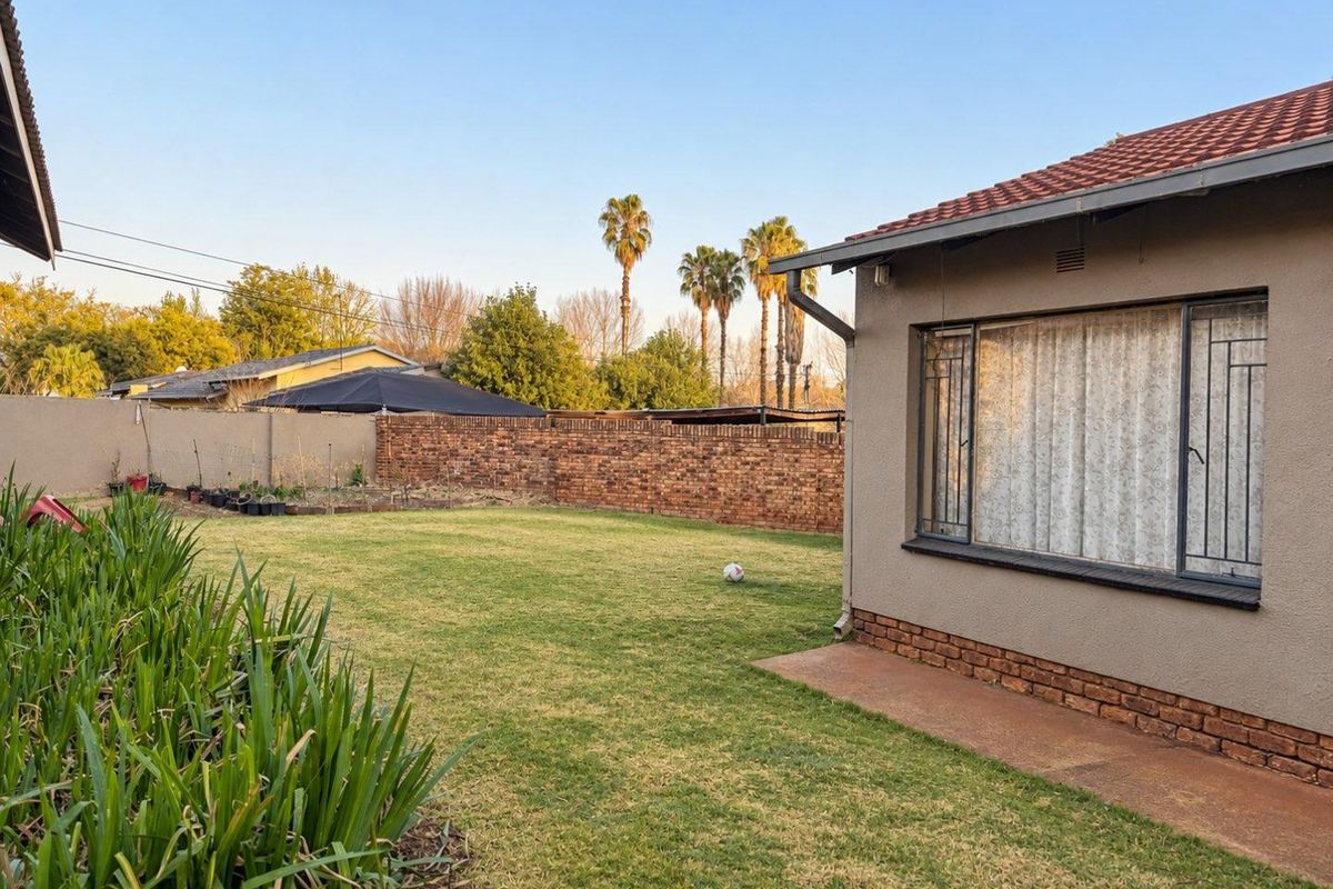 A spacious rear garden featuring a well-maintained lawn, brick boundary walls, and a paved pathway alongside the house exterior.