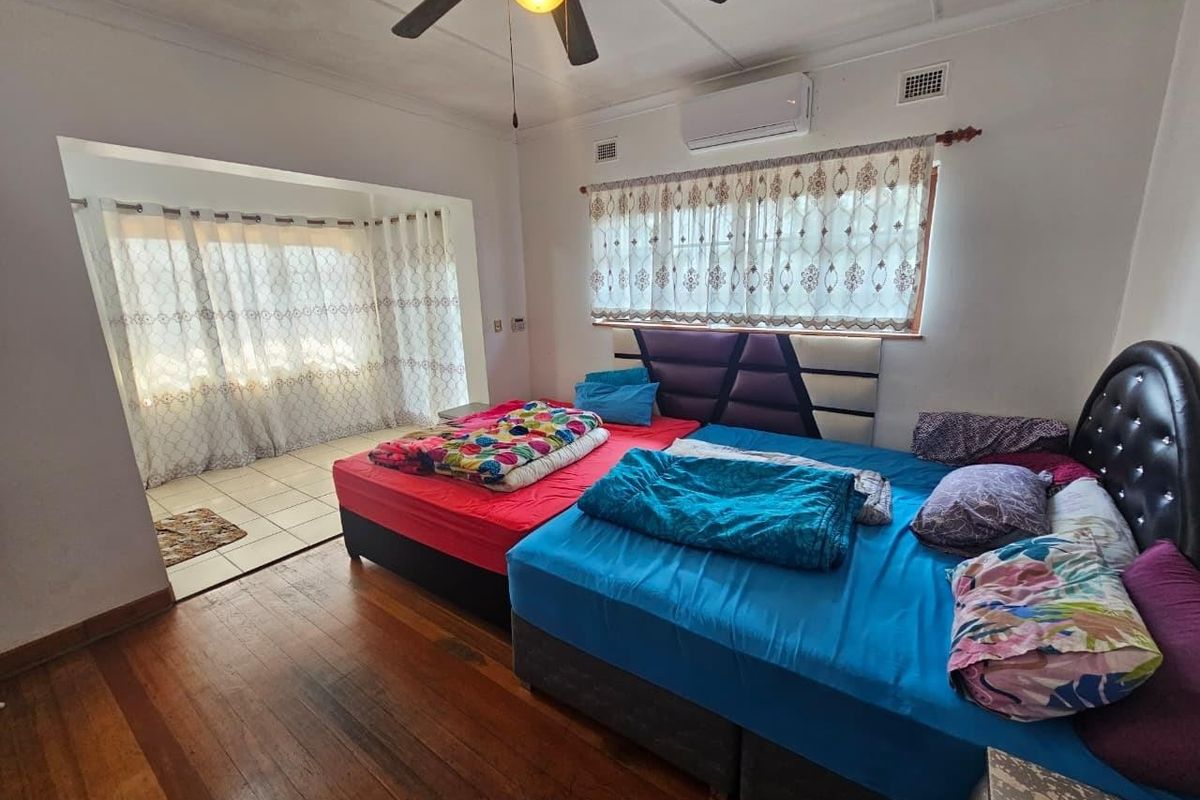 Spacious bedroom featuring hardwood flooring, a ceiling fan, and an integrated air conditioning unit, with an adjoining sunroom area.