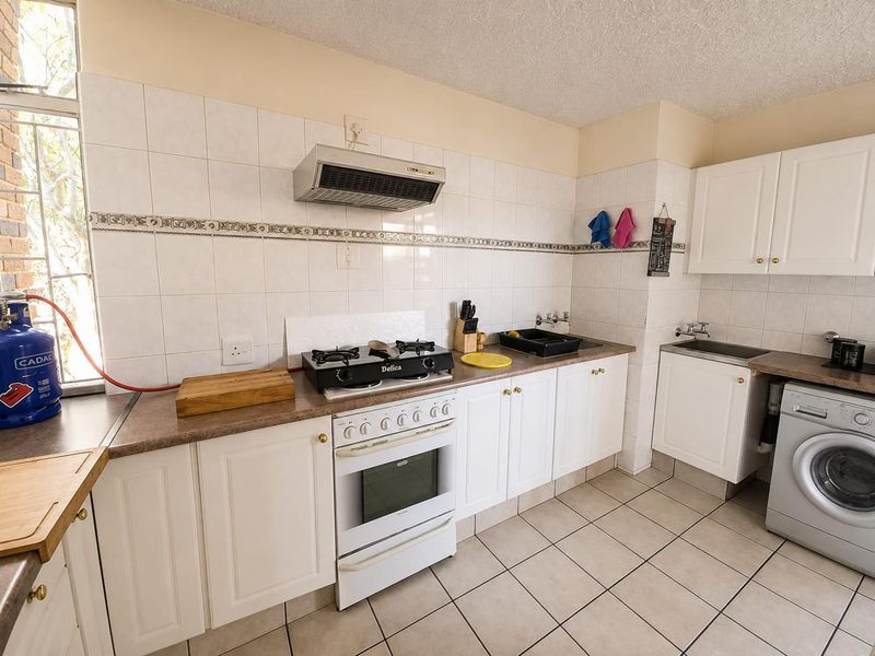 Functional kitchen featuring white cabinetry, laminate countertops, gas hob with extractor, and tiled splashbacks, providing a practical workspace with integrated laundry plumbing.