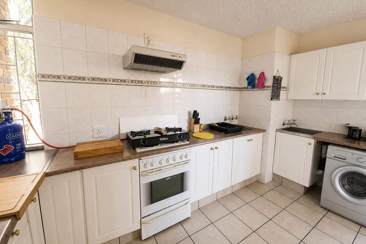 Functional kitchen featuring white cabinetry, laminate countertops, gas hob with extractor, and tiled splashbacks, providing a practical workspace with integrated laundry plumbing.