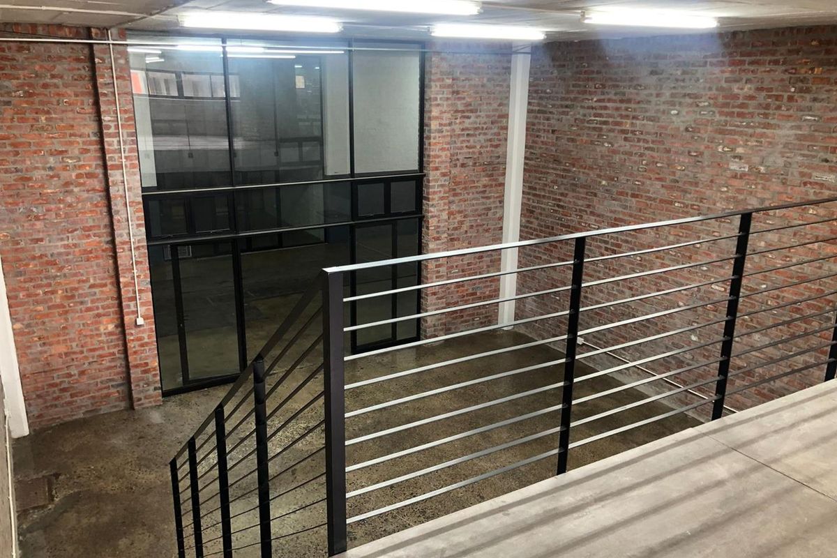 Spacious industrial-style interior featuring exposed brick walls, polished concrete floors, and a modern metal staircase railing overlooking the lower level.
