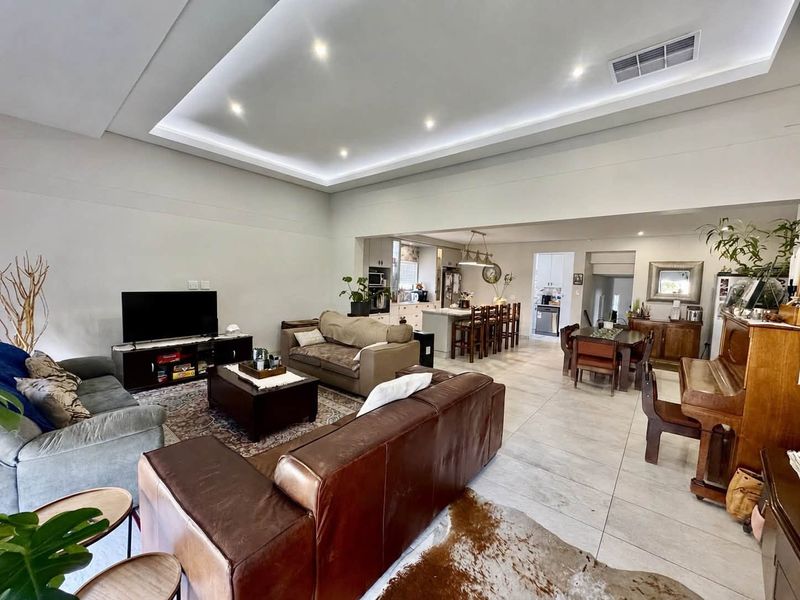 Spacious open-plan living area featuring a modern recessed ceiling with ambient lighting, tiled floors, and a seamless flow into the kitchen and dining space.