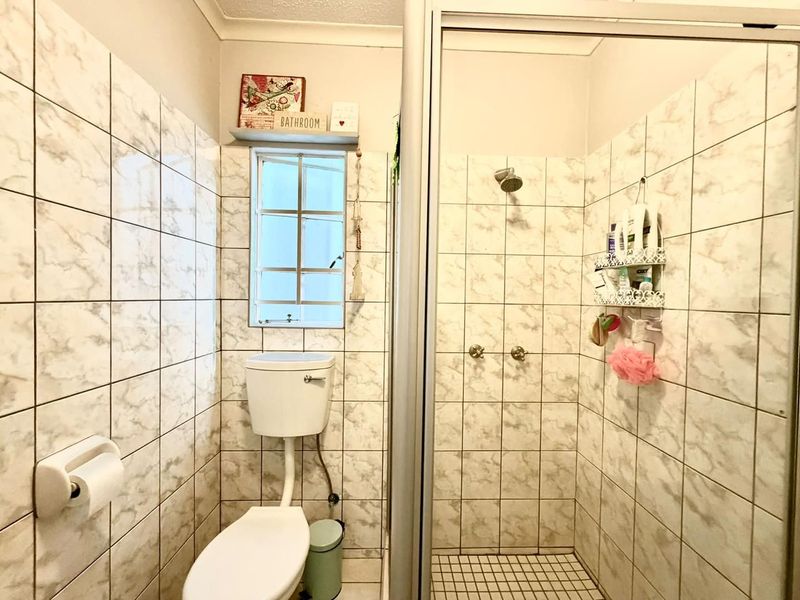 A functional bathroom featuring a shower enclosure, toilet, and marble-effect wall tiling throughout.