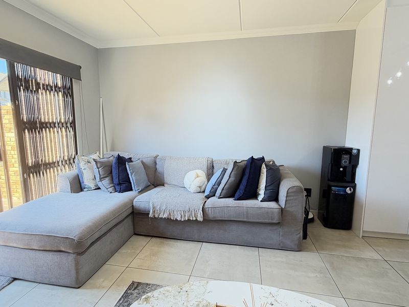A bright living room featuring large format floor tiles, a sliding glass door with security gate, and a built-in storage cupboard.
