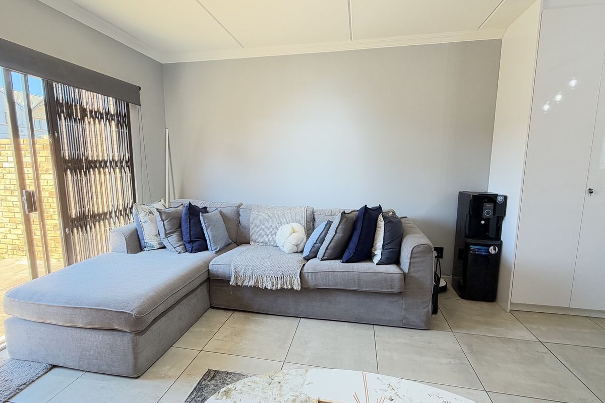 A bright living room featuring large format floor tiles, a sliding glass door with security gate, and a built-in storage cupboard.