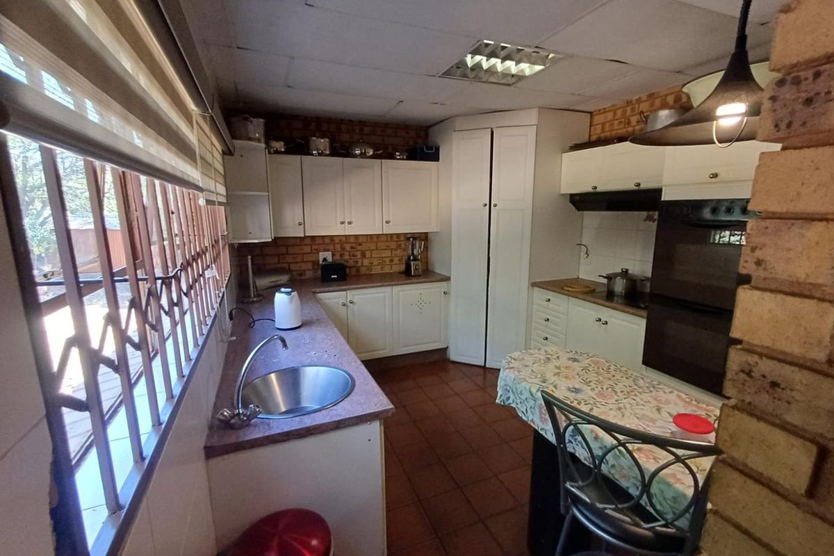 Functional kitchen featuring white cabinetry, built-in oven, stainless steel sink, and tiled flooring with large windows providing natural light.