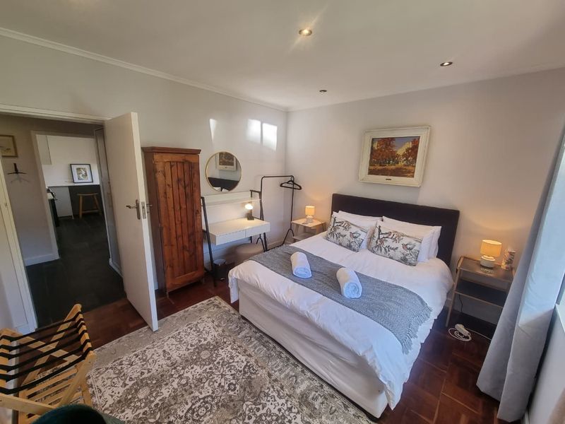 A well-maintained bedroom featuring polished wooden flooring, recessed ceiling lighting, and direct access to an adjacent room.