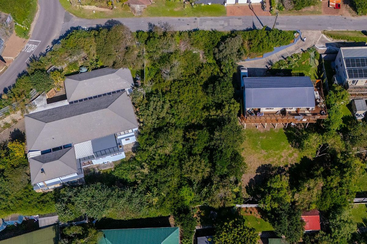 Aerial view of a residential plot featuring dense vegetation, situated between existing neighboring properties with established roof structures and access roads.