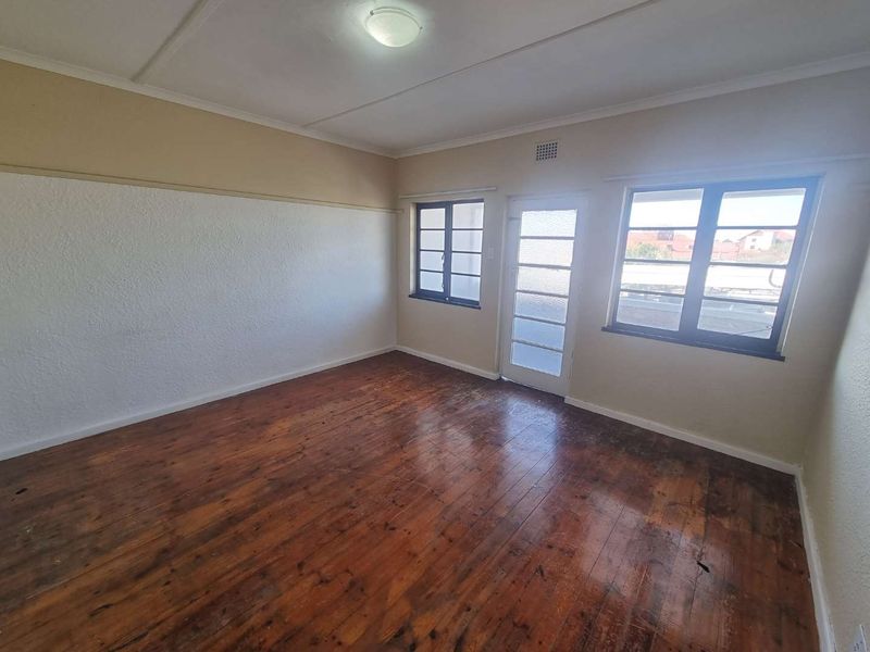 An empty bedroom featuring original timber flooring, large casement windows, and a glass panel door leading to an exterior space.