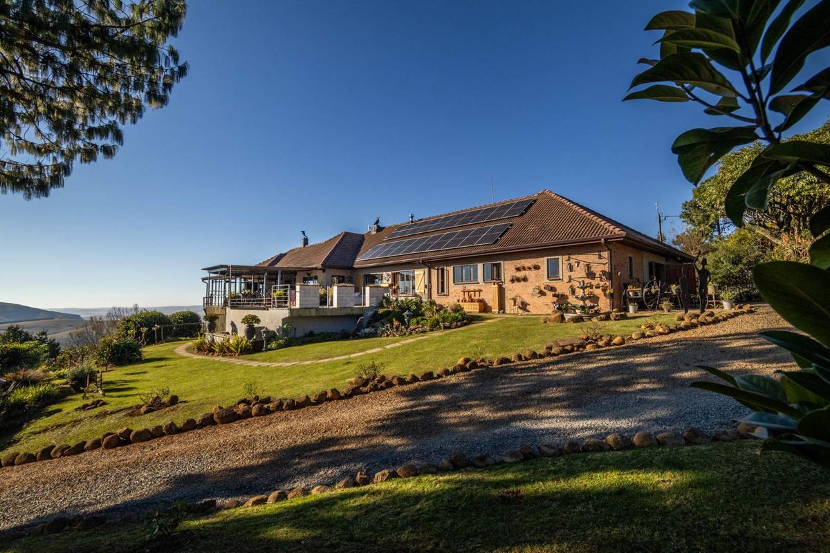 A well-maintained farm residence featuring a brick exterior, solar panel installation, and a spacious raised patio overlooking the surrounding landscape.