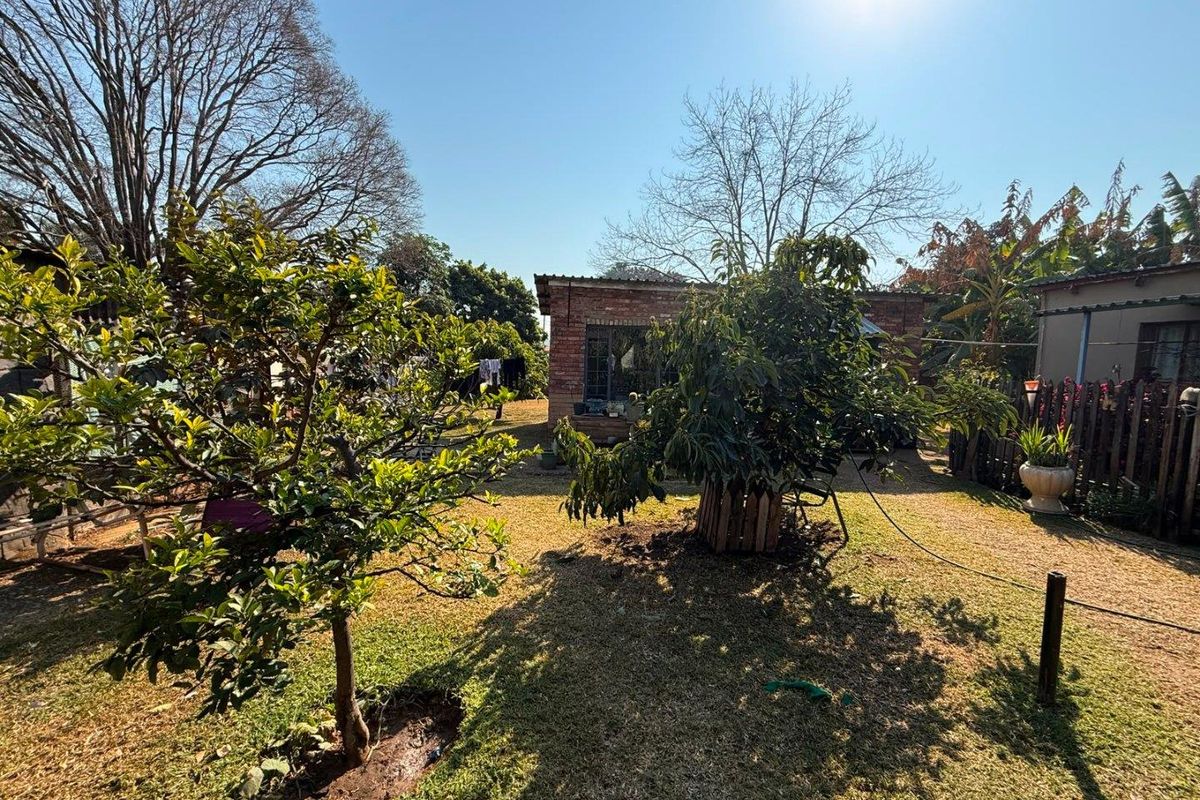A spacious rear garden featuring a brick outbuilding, established trees, and lawn area, providing a private outdoor space.