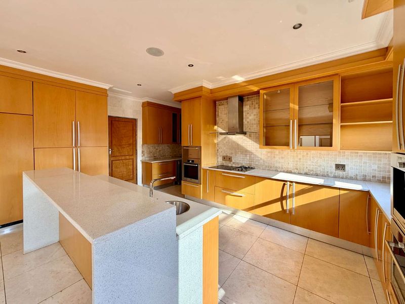 Spacious kitchen featuring light wood cabinetry, stone countertops, a central island, and integrated stainless steel appliances with a neutral tiled backsplash.