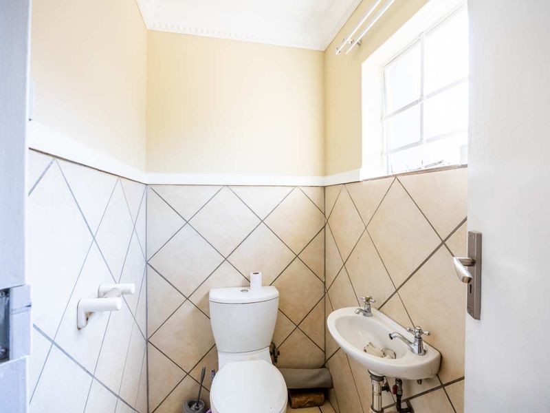 A compact guest bathroom featuring a toilet, wall-mounted basin, and neutral diamond-patterned wall tiles.