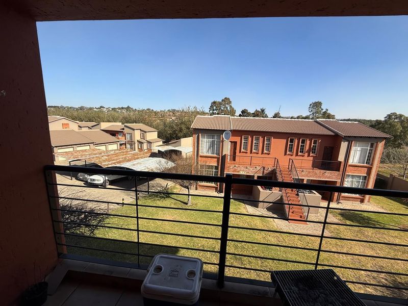 A covered balcony with a metal balustrade overlooking the apartment complex grounds and surrounding neighborhood.