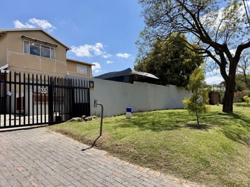 Front exterior view of the property featuring a paved driveway, metal security gate, and perimeter wall with visible maintenance requirements.