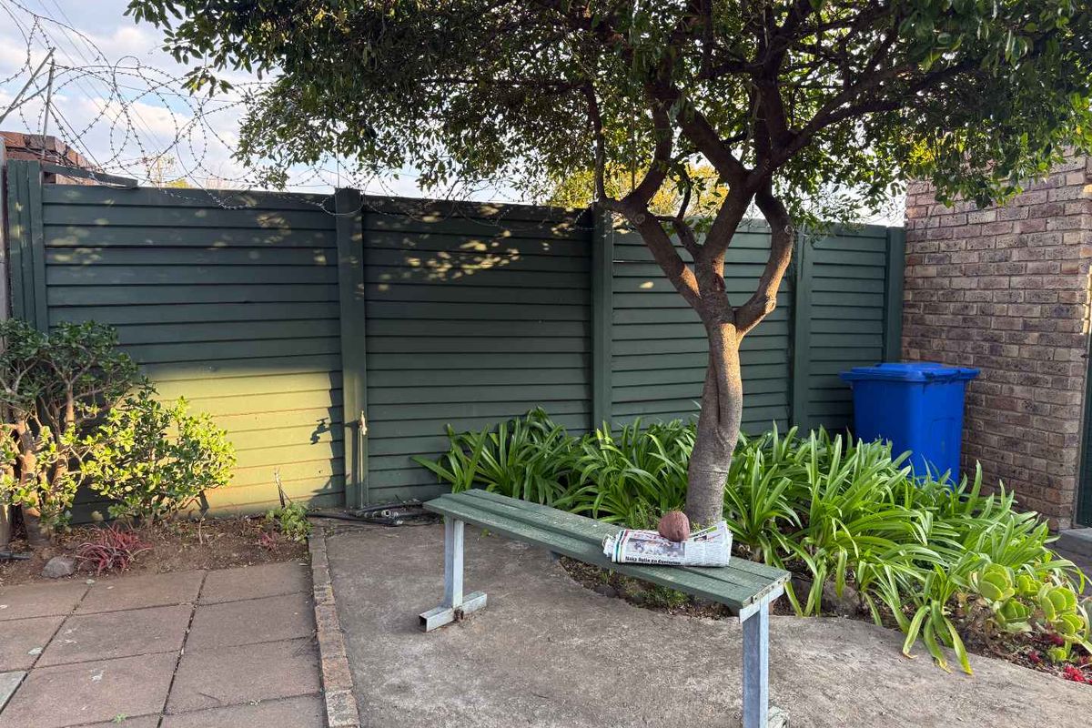 A private rear courtyard area featuring timber slat fencing with security razor wire, paved flooring, and established garden greenery.