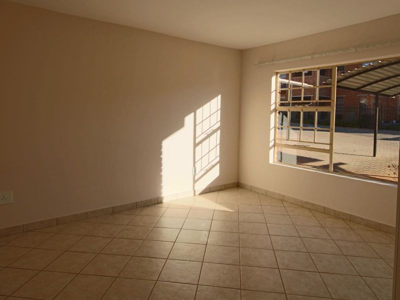 A bright, empty bedroom featuring neutral wall tones, tiled flooring, and a large window providing natural light and a view of the exterior area.