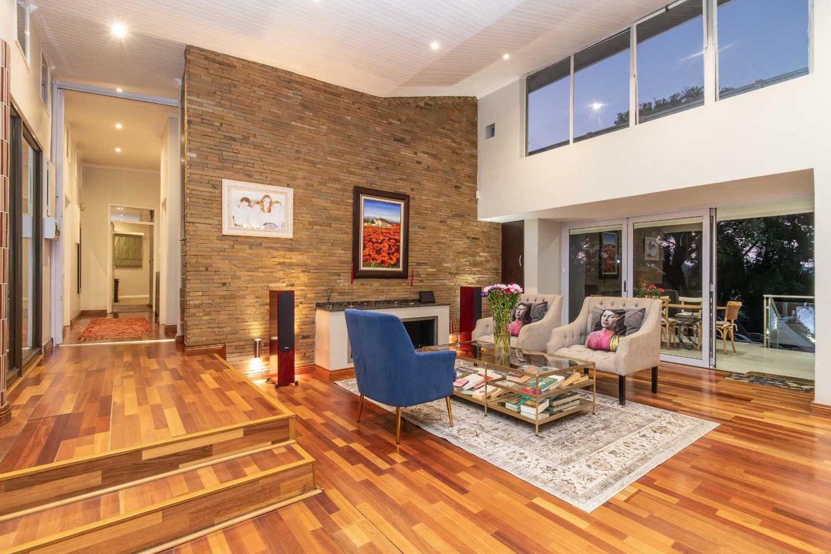 Spacious living room featuring a striking stone-clad feature wall, high vaulted ceilings, polished timber flooring, and large glass sliding doors leading to an outdoor area.