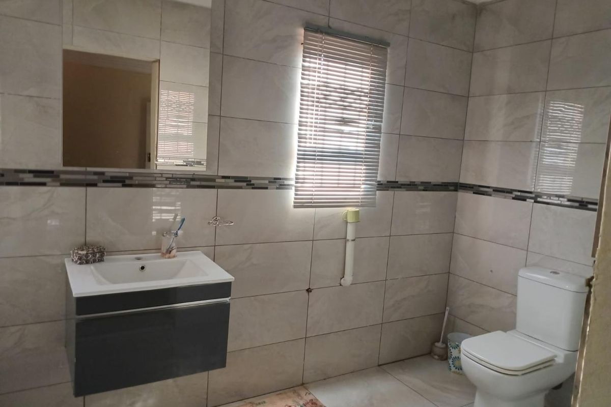 A functional bathroom featuring floor-to-ceiling wall tiles, a modern wall-mounted vanity with basin, a mirror, and a standard toilet.