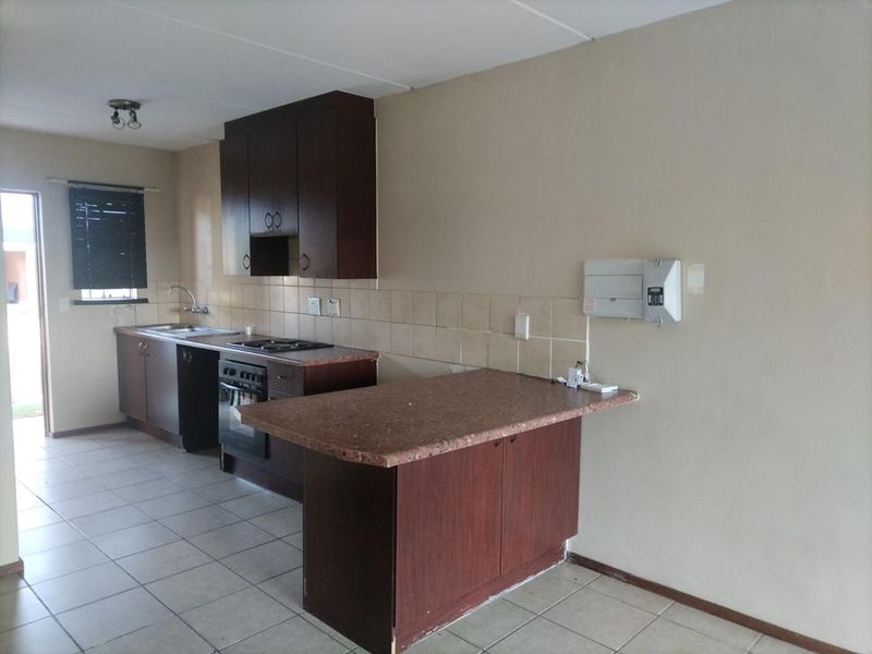 A functional kitchen featuring dark wood cabinetry, laminate countertops, built-in oven and hob, tiled backsplash, and tiled flooring in an open-plan layout.