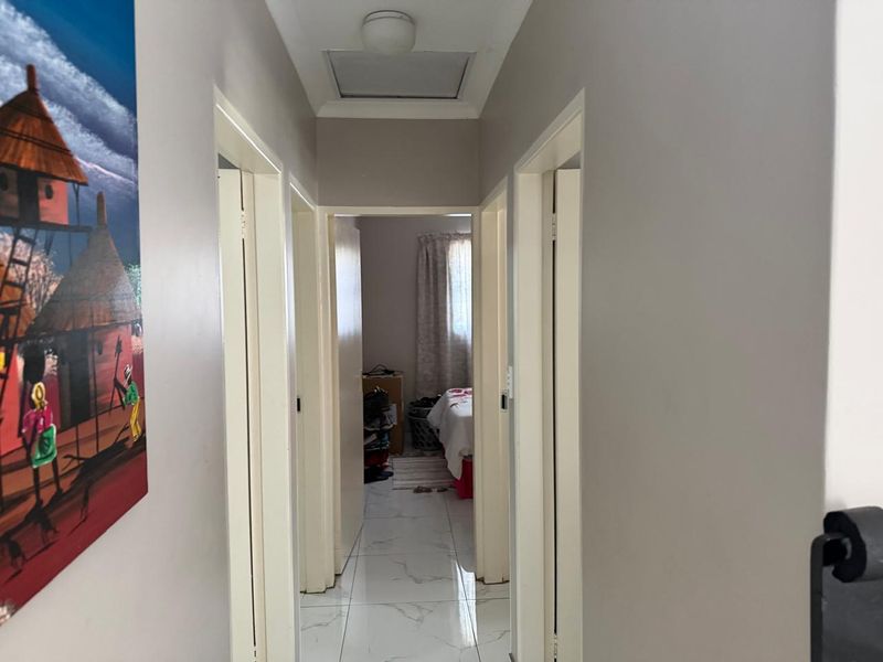 A clean, tiled hallway providing access to multiple rooms, featuring a neutral color palette and a ceiling access hatch.